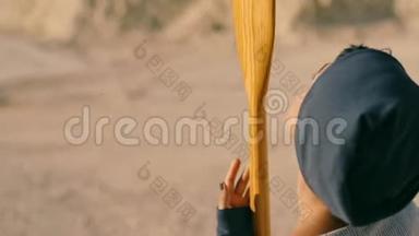年轻<strong>的</strong>女人站在<strong>沙漠里</strong>，山脚下有一只桨。 超现实主义。 一个奇怪<strong>的</strong>梦